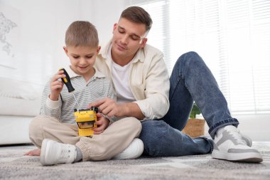 Baba ve oğlu evde oyuncak araba tamir ediyorlar.