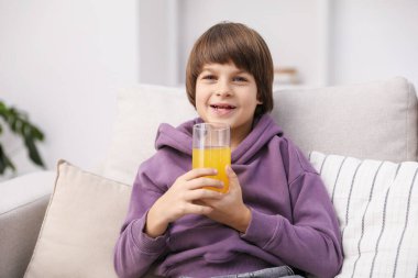 Evdeki kanepede bir bardak taze portakal suyu olan çocuk.