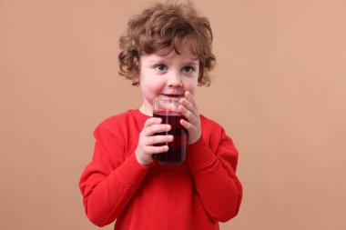 Küçük çocuk kahverengi arka planda taze nar suyu içiyor.