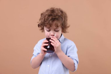 Küçük çocuk kahverengi arka planda taze nar suyu içiyor.