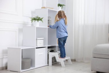 Evde çocuk güvenliği. Merdivendeki küçük kız, içerideki raf ünitesinde bir şeye uzanıyor.