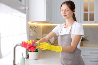 Evinde mikrofiber bezle mutfak musluğunu temizleyen kadın.