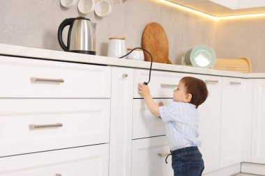 Evde çocuk güvenliği. Küçük çocuk mutfakta elektrikli su ısıtıcısına uzanıyor.