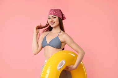 Pembe arka planda şişirilebilir yüzüklü mayo ve pantolon giymiş şık bir kadın.