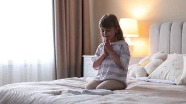 İncil 'i olan şirin küçük kız evde yatağında dua ediyor.