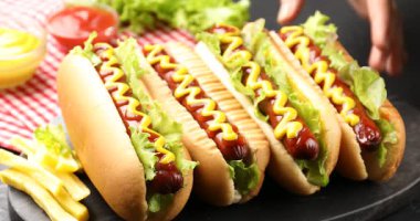 Bir kadın siyah masada ketçaplı, hardallı ve marullu lezzetli sosisli sandviç yiyor.