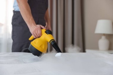 Haşere kontrol işçisi yatağı temizliyor, kapalı alanda buharlı temizleyiciyle, yakın plan. Metin için boşluk