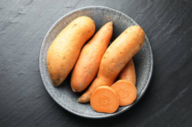 Tam ve tatlı patatesleri kasede, koyu dokulu masada, üst tarafta.