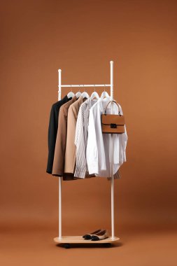 Askıda asılı farklı kıyafetler, çanta ve ayakkabılar kahverengi arka planda