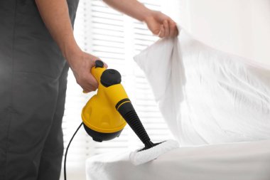 Haşere kontrol işçisi yatağı temizliyor, kapalı alanda buhar temizleyicisiyle, yakın plan