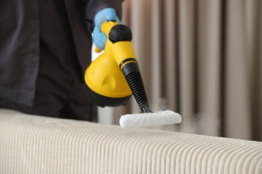 Haşere kontrol görevlisi kanepeyi temizliyor, kapalı alanda buharlı temizleyici ile, yakın plan. Metin için boşluk