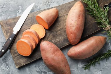 Çiğ patates, biberiye, ahşap tahta ve bıçak dokulu gri masa, düz yatıyordu.