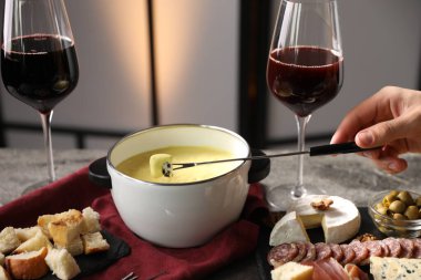 Bir kadın peyniri fondü kabına (caquelon) bandırıyor. Eritilmiş peyniri kapalı bir masada, yakın plan.