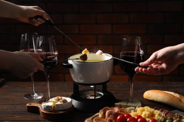 Kadınlar farklı aperatifleri fondü tenceresine (caquelon) daldırıyor. Eritilmiş peynirle kapalı masa içinde, yakın plan.