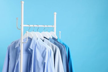 Açık mavi arka planda askıda asılı farklı kıyafetler, yakın plan. Metin için boşluk