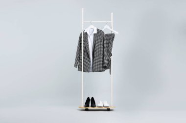 Farklı giysiler askıda asılı ve ayakkabılar açık gri arka planda