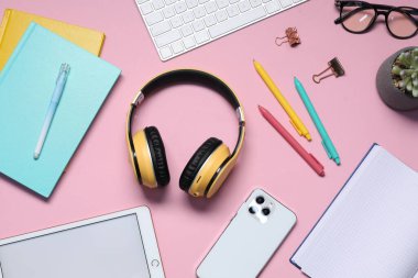 Kulaklıklar, akıllı telefon, tablet, çiçek dekoru, pembe arka planda gözlük ve kırtasiye malzemesi, düz konum