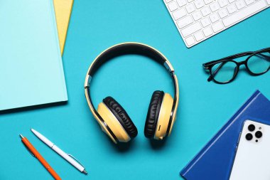 Açık mavi arkaplan üzerinde kulaklık ve kırtasiye ile düz kompozisyon yatıyordu