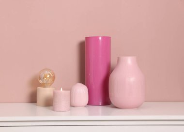 Farklı güzel vazolar, yanan mum ve lamba, kapalı alandaki bej duvarın yanındaki dolapta.