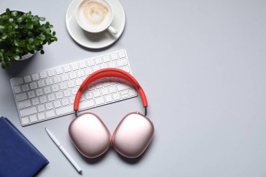 Kulaklıklar, bilgisayar klavyesi, kahve, kırtasiye malzemeleri ve açık gri arka planda çiçek dekoru, düz yatak. Metin için boşluk
