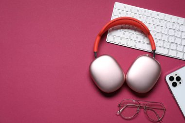 Kulaklıklar, akıllı telefon, bilgisayar klavyesi ve kırmızı arka planda gözlük, düz konum. Metin için boşluk