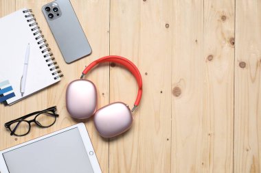 Kulaklıklar, akıllı telefon, tablet, bardaklar ve kırtasiye malzemeleri ahşap masa, düz yatak. Metin için boşluk