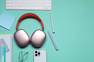 Kulaklıklar, bilgisayar klavyesi, akıllı telefon ve turkuaz arka planda kırtasiye malzemesi. Metin için boşluk