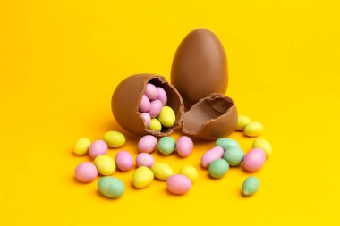 Sarı arka planda renkli şekerli lezzetli çikolata yumurtaları. Mutlu Paskalyalar
