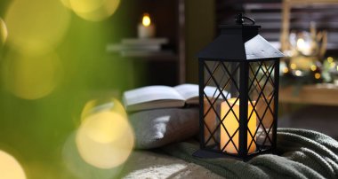 Kapalı alanda yanan mum ve battaniyeli Noel feneri, yakın plan. Bokeh etkisi