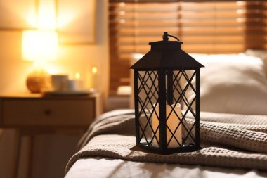 Beautiful Christmas lantern with candle on bed indoors. Space for text