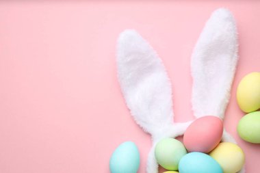 Mutlu Paskalyalar. Tavşan kulaklı şirin saç bandı ve pembe arka planda yumurta boyası, düz yatak. Metin için boşluk