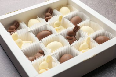 Paskalya kutlaması. Çikolata yumurtaları ve tavşanlar gri desenli masada kutuda, yakın plan.