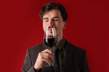 Profesyonel şarap garsonu kırmızı arka planda şarap tadıyor.
