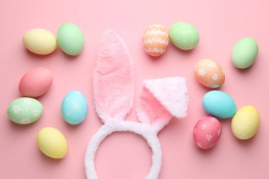 Tavşan kulaklı şirin saç bandı ve pembe arka planda Paskalya yumurtaları, düz yatış.