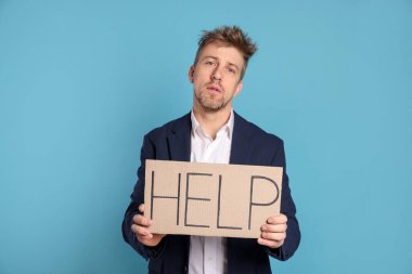 Mutsuz işadamı elinde kelime yazılı karton tabela tutuyor Açık mavi arka planda yardım