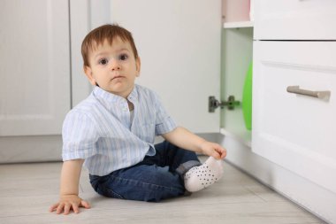 Evde çocuk güvenliği. Küçük çocuk mutfakta temizlik ürünleriyle dolap açıyor.