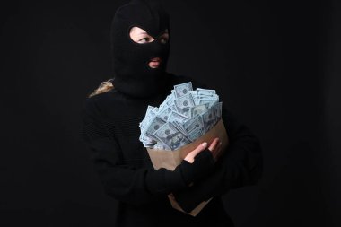 Siyah arka planda çanta dolusu parası olan maskeli bir hırsız.