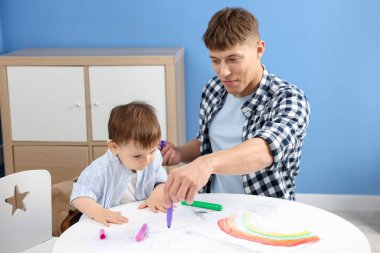 Erkek dadı ve küçük şirin çocuk beyaz masaya resim çiziyorlar.