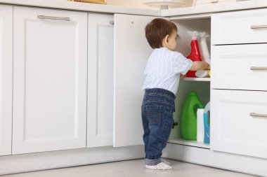 Evde çocuk güvenliği. Küçük çocuk mutfakta temizlik ürünleriyle dolap açıyor.