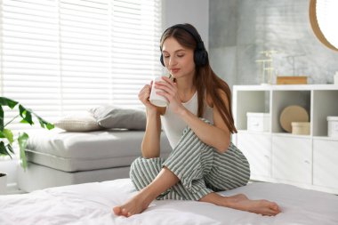 Kahveli güzel bir kadın evde yatağında müzik dinliyor.