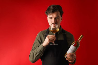 Profesyonel şarap garsonu kırmızı arka planda şarap tadıyor.