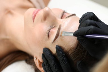 Güzellik uzmanı, kalıcı kaş makyajı prosedüründen önce kadının yüzüne işaretler çiziyor.