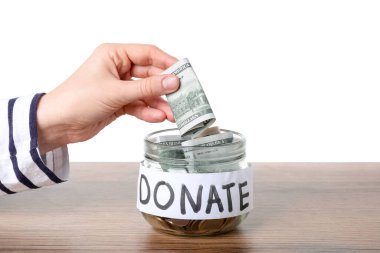 Bir kadın bağış kavanozuna dolar koyuyor ahşap zeminde beyaz arka planda, yakın plan.