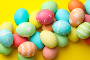 Many painted Easter eggs on yellow background, flat lay