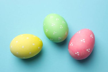 Many painted Easter eggs on light blue background, flat lay