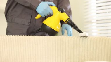 Haşere kontrol işçisi kanepeyi temizliyor. Kapalı alanda buhar temizleyicisi var.