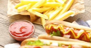 Ahşap masada soslu, marullu ve patates kızartmalı lezzetli sosisliler, yakın plan. Kamera aşağı iniyor