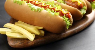 Ketçaplı lezzetli sosisliler, hardal, marul ve patates kızartması, yakın plan. Kamera yukarı hareket ediyor