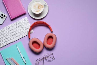 Kulaklıklar, akıllı telefon, bilgisayar klavyesi, mor arka planda kahve ve kırtasiye malzemesi, düz konum. Metin için boşluk