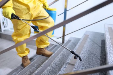 Koruyucu giysili haşerat kontrol işçisi merdivenlere böcek ilacı sıkıyor, seçici bir odak noktası. Metin için boşluk